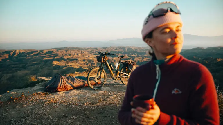 Bikepacking setup on a cliffside with an e bike, sleeping bag, and warm morning light.
