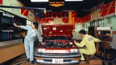 Two Bosch technicians working on a red Honda Civic in a Bosch service center, using diagnostic equipment.