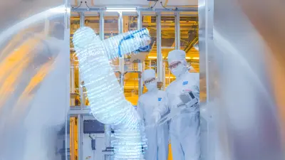Two employees work together on a machine in the new chip factory in Dresden. The graphic integration of code symbolises artificial intelligence.