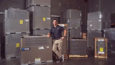 Customer service representative Eric Lander is standing in a warehouse, leaning against a York cooling unit. In the background, more packaged units are visible.