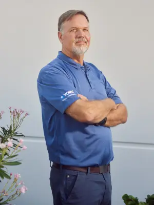Steven Edwards stands with arms crossed, wearing a blue polo shirt with a "YORK" logo on the sleeve and dark blue pants.