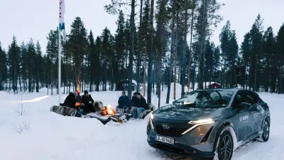 Mehrere Personen sitzen um ein Lagerfeuer im Schnee.