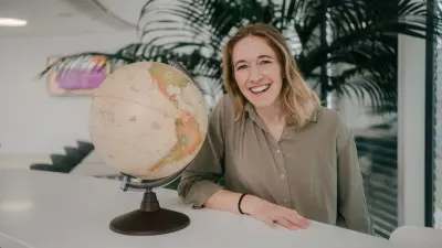 Das Bild zeigt Bosch Mitarbeiterin Katharina. Sie steht neben einer Weltkugel in einer Büroumgebung und lächelt in die Kamera.