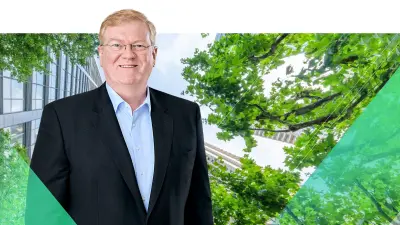 Bosch CEO Stefan Hartung stands in front of a high-rise landscape with trees photographed from below.