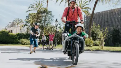 A man is transporting a child on a cargo eBike and brakes sharply because a skateboard rolls into the path.