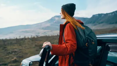 A woman standing next to a car and looking into the landscape.