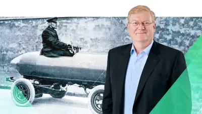 Portrait of Bosch CEO Stefan Hartung, in the background an archival photograph of an racer in the electric-powered speed record car La Jamais Contente.