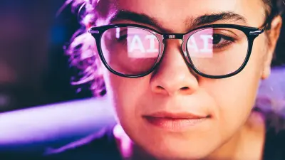 Woman using artificial intelligence technology on laptop with glasses reflection.