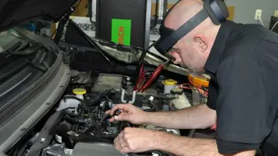 A man repairs an engine in a car using the Technician Process Assistant from Bosch.