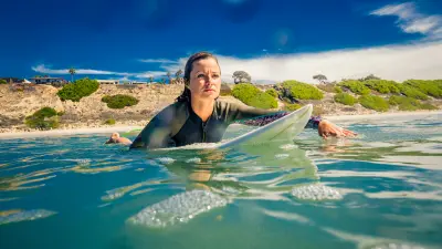The image shows a women on a surfboard in the water.