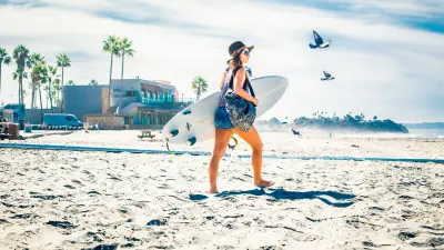 The images shows a women with a surfboard at the beach.