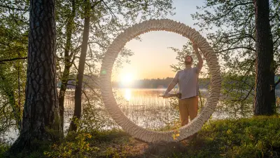 Der Skulpturenkünstler Adam Detre steht im Wald am Ufer eines Sees vor seinem neuen Kunstwerk – einem riesigen Ring aus Holz, in den kunstvoll Muster geschnitzt sind. Adam hält in der rechten Hand einen Bosch Professional Geradschleifer. Er betrachtet seine Skulptur und berührt diese vorsichtig mit der linken Hand. Im Hintergrund geht die Sonne über dem See auf. Die Sonnenstrahlen scheinen durch den Ring.