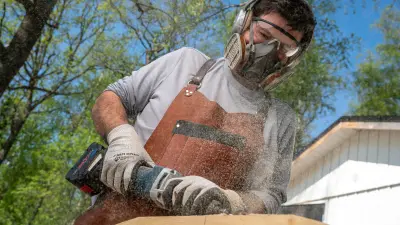 Wood artist Adam Detre grinds a piece of wood out in the forest with a GGS 18V-10 SLC Professional straight grinder from Bosch. Flying sawdust can be seen.