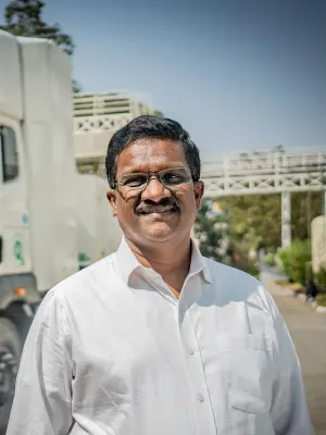 George Anthony, a man with dark hair, a mustache, and glasses, wearing a white collared shirt, smiles warmly.