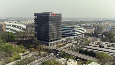 An aerial shot from a high vantage point captures a sprawling cityscape under a hazy sky, centered on a modern, multi-story building prominently displaying the red "BOSCH" logo on its upper facade.