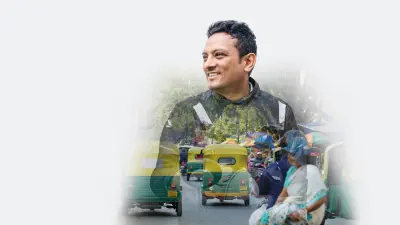Sandeep C D, a man with dark hair in a motorcycle outfit looking confidently at the camera. His portrait is superimposed over a traffic scene with street traffic in India including yellow and green autorickshaws in the background.