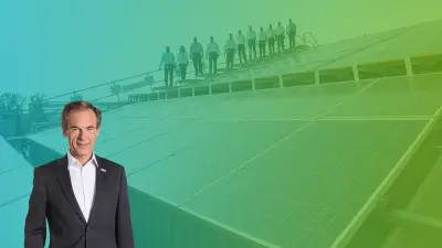 Volkmar Denner, CEO Bosch, steht vor einem grünen Hintergrund, der Mitarbeitern auf einem Dach stehend im Hintergrund zeigt.