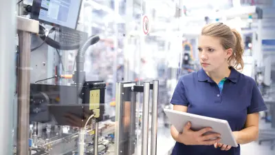 Eine Frau in einer Fertigungshalle mit Tablet in der Hand