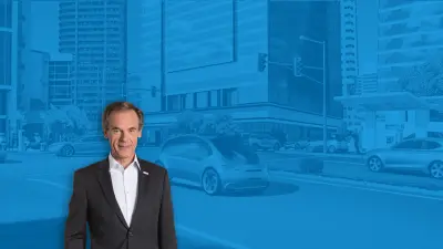 Volkmar Denner, CEO Bosch, stands against a blue background that shows a street with many cars and a gas station in the background.