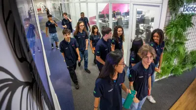 Numerous young people in the same dark blue short on the aisle of a building talking to each other.