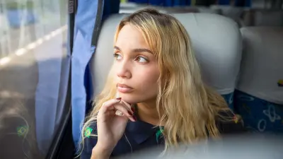 Young woman sits at the window of a bus and looks out of the window.