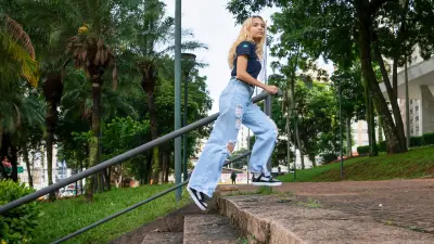 Young woman with long blond hair and dark blue shirt takes a big step on a staircase. In the background, trees and a white building can be seen.