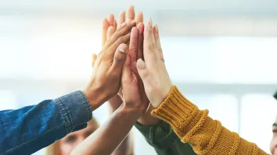 Employees of different skin colors hold their hands together in the middle