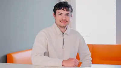 Testimonial Jonas sitzt auf einem orangenen Sofa und lächelt in die Kamera.