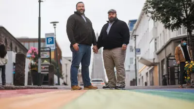 Alfons Müller und sein Ehemann Robby stehen händchenhaltend auf der Straße.