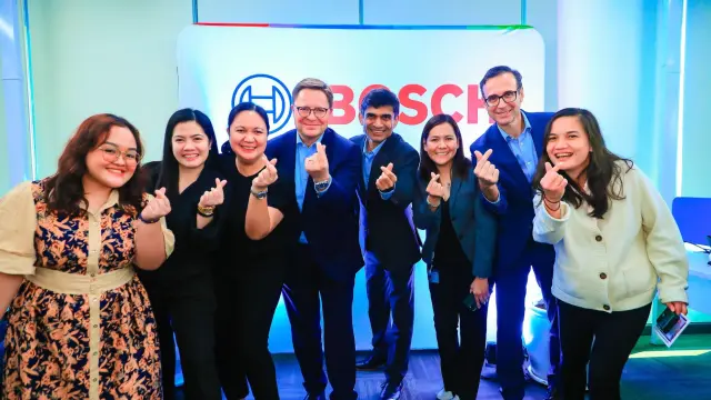 Chloie together with seven people smiles at the camera and makes a gesture with their hands.