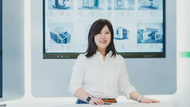 Lei from China stands behind a table and smiles at the camera.