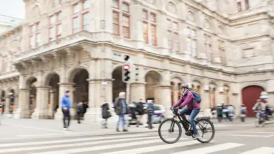 Eine Radfahrerin im städtischen Verkehr. Sie fährt an einem Zebrastreifen mit Passanten vorbei.