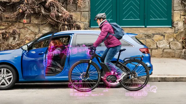 Eine Frau fährt mit ihrem Fahrrad eng an einem Auto vorbei. Sie steht in der Gefahr, in die soeben geöffnete Autotür zu fahren.