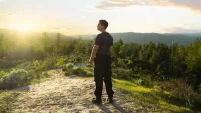 Firefighter Ricky Staley stands on a hill above the forest. Illuminated by the evening sun, he looks off into the distance.