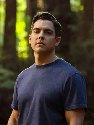 A muscular man wearing a blue t-shirt is standing in the woods. The portrait shows firefighter Ricky Staley.