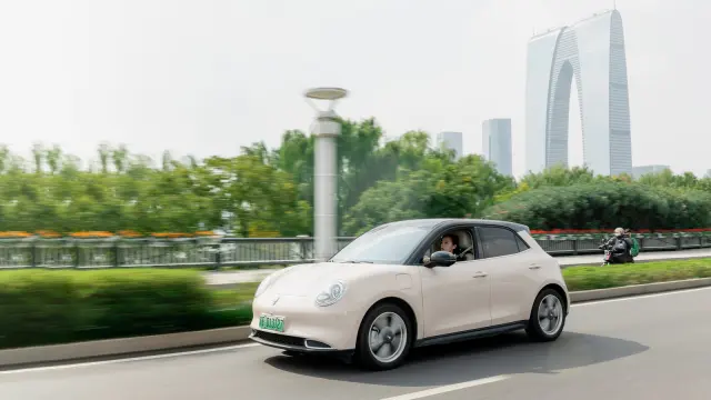 A street view of Cao Mengyi in her Ora Good Cat on the way to work; in the background the skyline of Suzhou is visible in front of water.