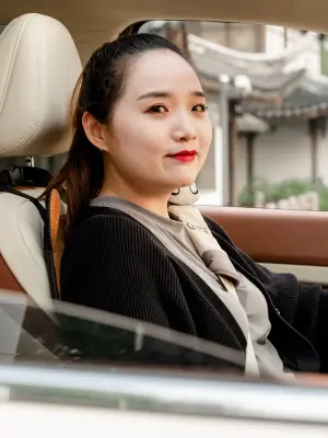 Cao Mengyi sits behind the wheel of her Ora Good Cat with her gaze directed at the camera.