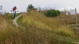 Mountain biker riding down a narrow trail through tall grass.