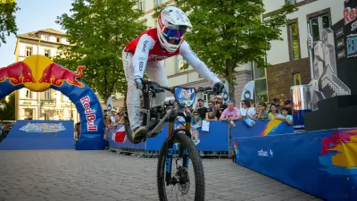 Mountain biker riding past spectators at a Red Bull event in a city street.