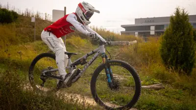 Mountain biker riding a Commencal bike on a narrow trail through grassy terrain.