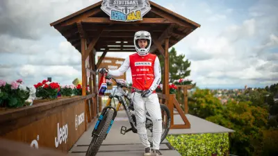 Mountain biker standing with a bike on a wooden start platform overlooking Stuttgart.