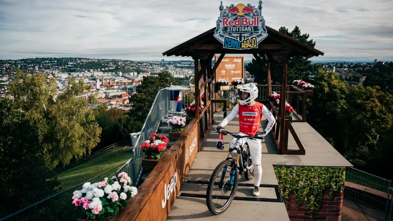 A mountain biker in full racing gear stands with his e-bike on a wooden starting ramp, ready for the Red Bull Cerro Abajo race in Stuttgart.