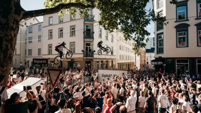 Two mountain bikers jumping above a crowded city street lined with spectators.