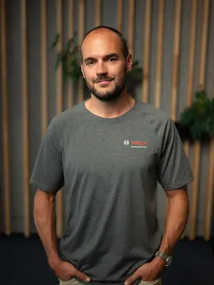 Portrait of a person wearing a gray Bosch T-shirt in front of a wooden slat wall.