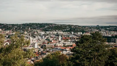Panoramic view over Stuttgart with buildings, wooded hills and trees in the foreground.