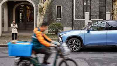 Ein Kurierfahrer fährt auf dem Fahrrad vor dem emissionsfreien NIO ES8.