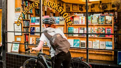 The image shows Maggie on her eBike in front of a bookstore.