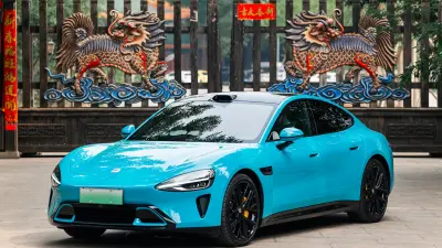 A bright blue electric car with a black roof is parked in front of a traditional Chinese wooden gate.