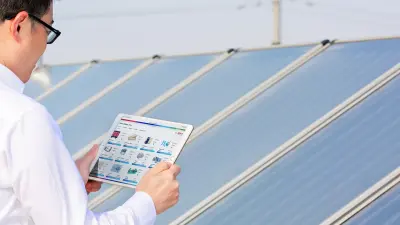 Bosch-Mitarbeiter Honghui Wu schaut auf sein Tablet. Es sind unterschiedliche Werte und Schaubilder zu sehen. Im Hintergrund sind Solarthermie-Panels zu erkennen.