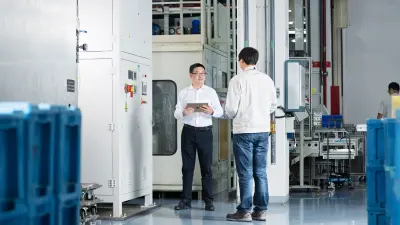 Bosch-Mitarbeiter Honghui Wu steht mit einem Kollegen vor einer großen Maschine. In der Hand hält er ein Tablet.